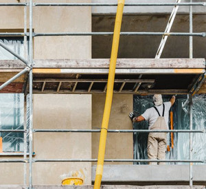 Ein Bauarbeiter klebt die Fenster mit Folie ab er will die Fassade streichn