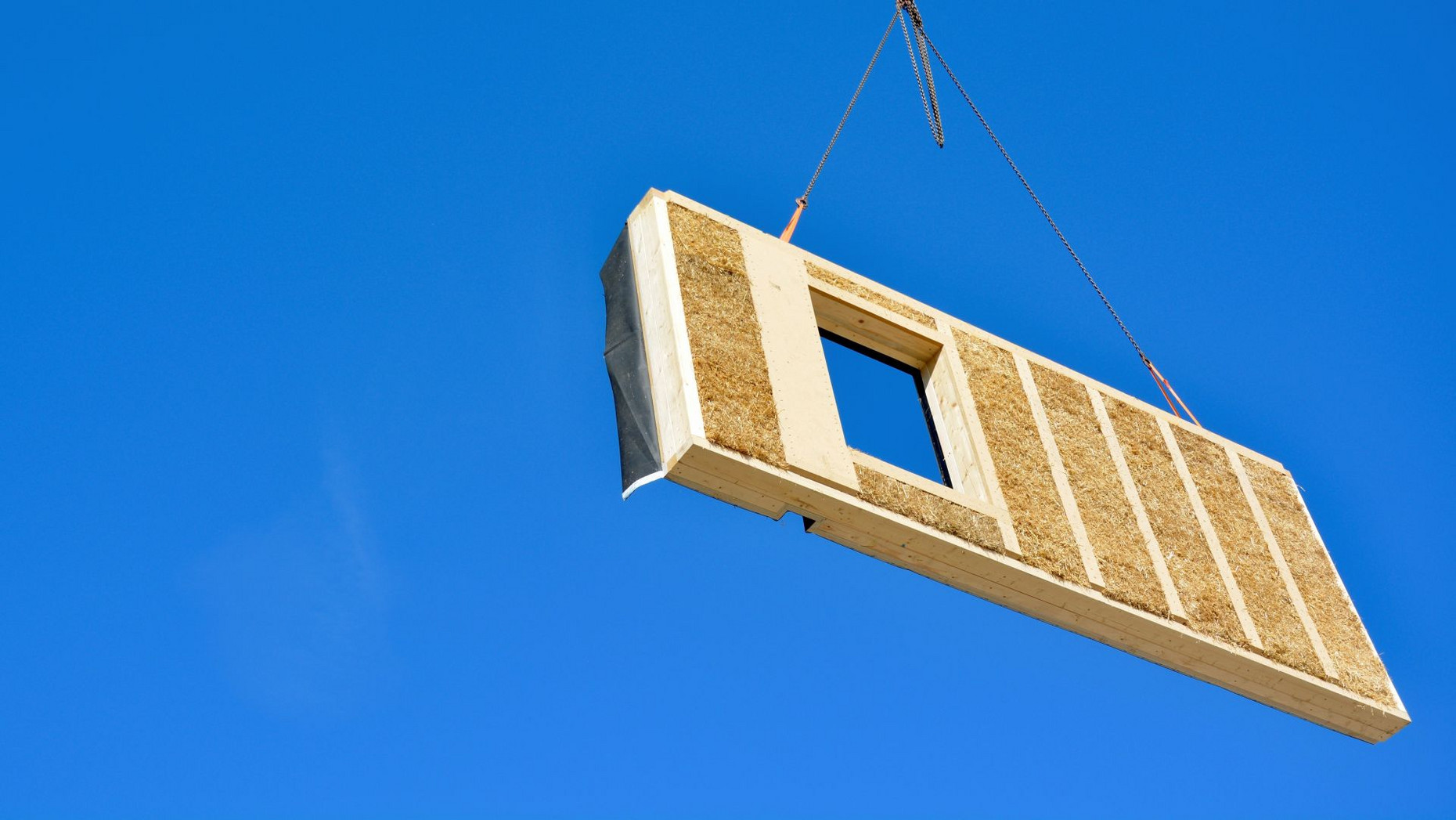 Holzstrohbauelement am Kran vor blauem Himmel